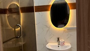 Un baño con cabina de ducha de vidrio, lavamanos blanco con espejo y paredes con estampado de mármol.