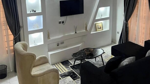 Una sala de estar moderna con un televisor de pantalla plana montado en la pared, un sillón color beige, un sofá negro y una mesa de centro.