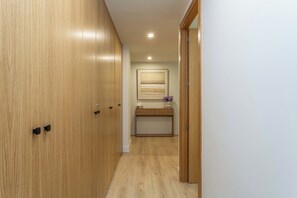 Um corredor com portas de madeira, uma pequena toucador com espelho e um candeeiro no teto.
