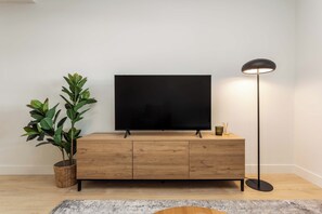 A flat-screen TV on a wooden cabinet, a floor lamp, and a potted plant. - A quietly luxurious three-bedroom in Chamartín, Madrid's most upscale family neighborhood, close to the northern business district and well connected to the rest of the city. (MADRID)