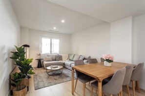 A modern living room with a sofa, a dining table with chairs, a coffee table, and a potted plant. - A quietly luxurious three-bedroom in Chamartín, Madrid's most upscale family neighborhood, close to the northern business district and well connected to the rest of the city. (MADRID)