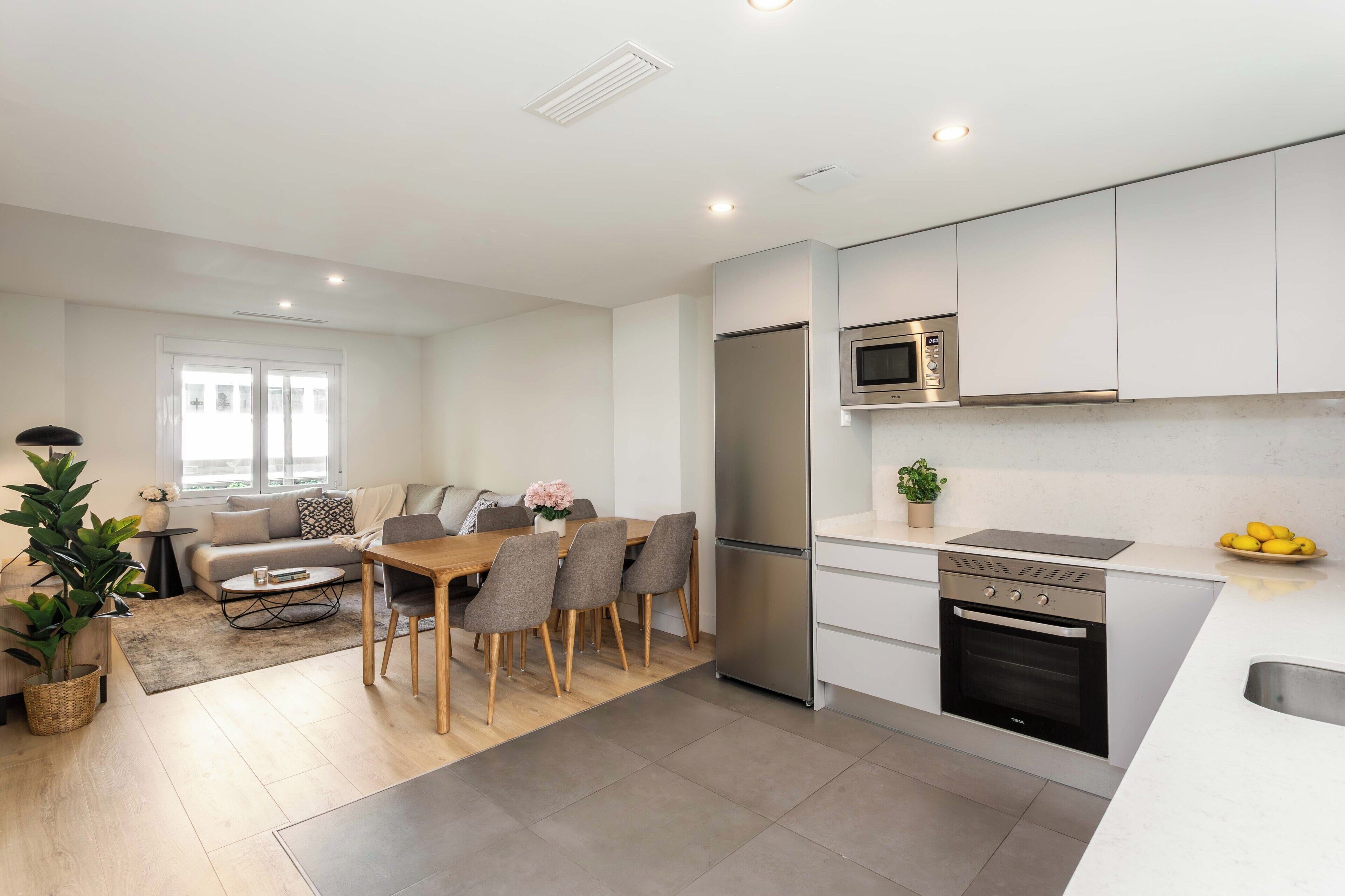A modern kitchen with a built-in oven, microwave, and refrigerator. There is a dining area with a table and chairs.