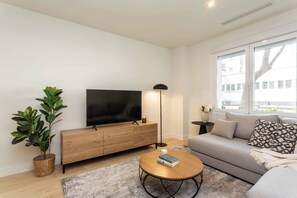 Ein modernes Wohnzimmer mit Flachbildfernseher, Holzkonsole, rundem Couchtisch und einer Couch mit Kissen.