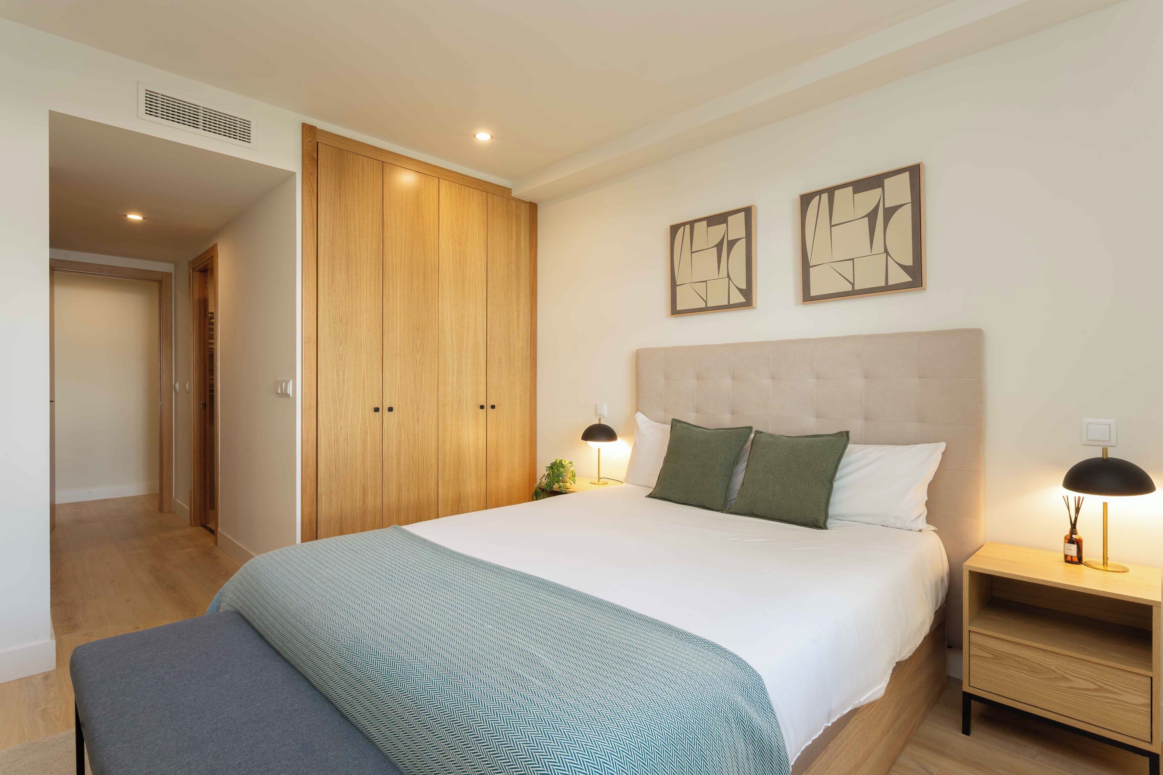 Una camera da letto con un letto grande, un armadio in legno, due elementi decorativi a parete, un comodino con una lampada e una panca.