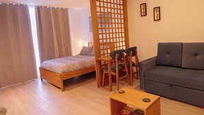 Ein Zimmer mit einem Bett, einem grauen Sofa, einem Holztisch und einer Raumtrennung.