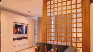 Ein modernes Wohnzimmer mit Flachbildfernseher, Holzmöbeln und einem dekorativen Raumteiler.