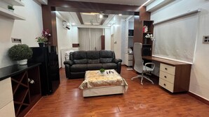 A modern living room with a leather sofa, a coffee table, and a TV. There are shelves with plants and a desk with a chair. - Atlas Homes Penthouse 1BHK Jacuzzi @ Hitech City (Hyderabad)