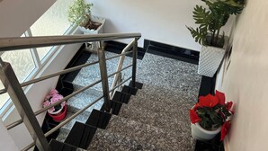 A staircase with a metal railing, potted plants, and a window with a decorative pattern. - Atlas Homes Penthouse 1BHK Jacuzzi @ Hitech City (Hyderabad)