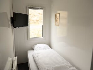 A small, single-bed room with a window, a mounted television, and a framed picture on the wall. - Mobile Home Park (Strendur)