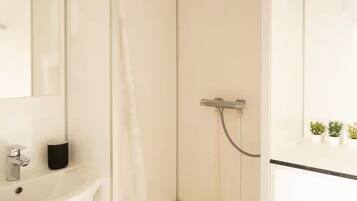 A bathroom with a white sink, a mirror, and a shower with a handheld showerhead.