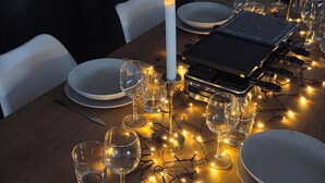 A dining table set with plates, glasses, and a candle, surrounded by string lights. - COZY APARTMENT IN FORMIGUERES, SLEEPS 6–8 (Formiguères)