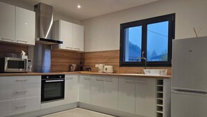 A modern kitchen with white cabinets, stainless steel appliances, a window with a view, and a built-in oven. - COZY APARTMENT IN FORMIGUERES, SLEEPS 6–8 (Formiguères)