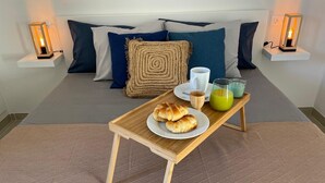 A neatly made bed with pillows, a bedside table with a lamp, a tray with croissants, a cup, and a glass of juice. - Casa Dante, Las Palmeras III apartments (Tías)