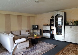 Una sala de estar con un sofá, una mesa de centro, un televisor, una estantería y un aparador.