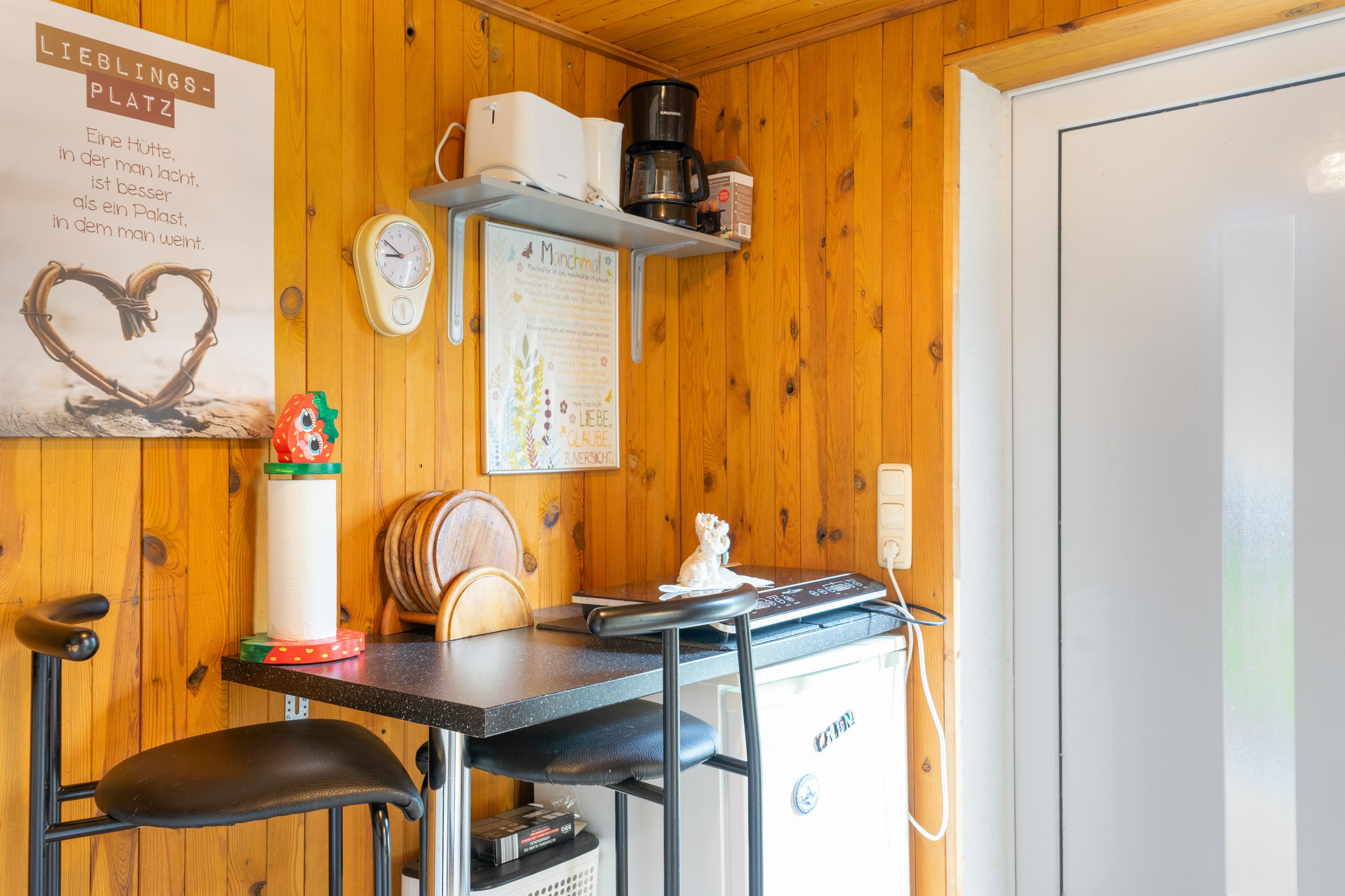 A kitchen with wooden walls, a coffee machine, a clock, and a heart-shaped decoration.