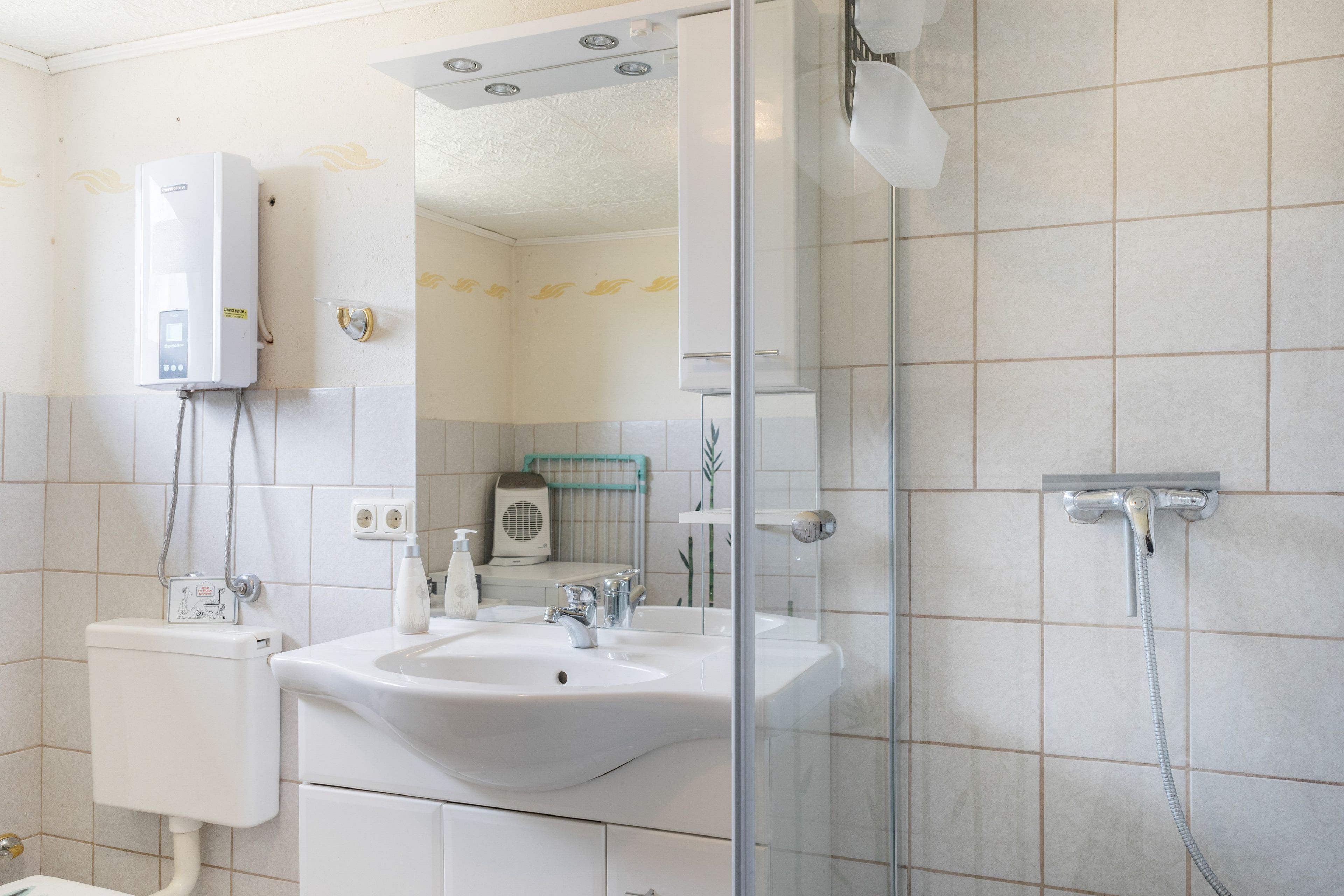 A bathroom with a sink, mirror, shower, and toilet.