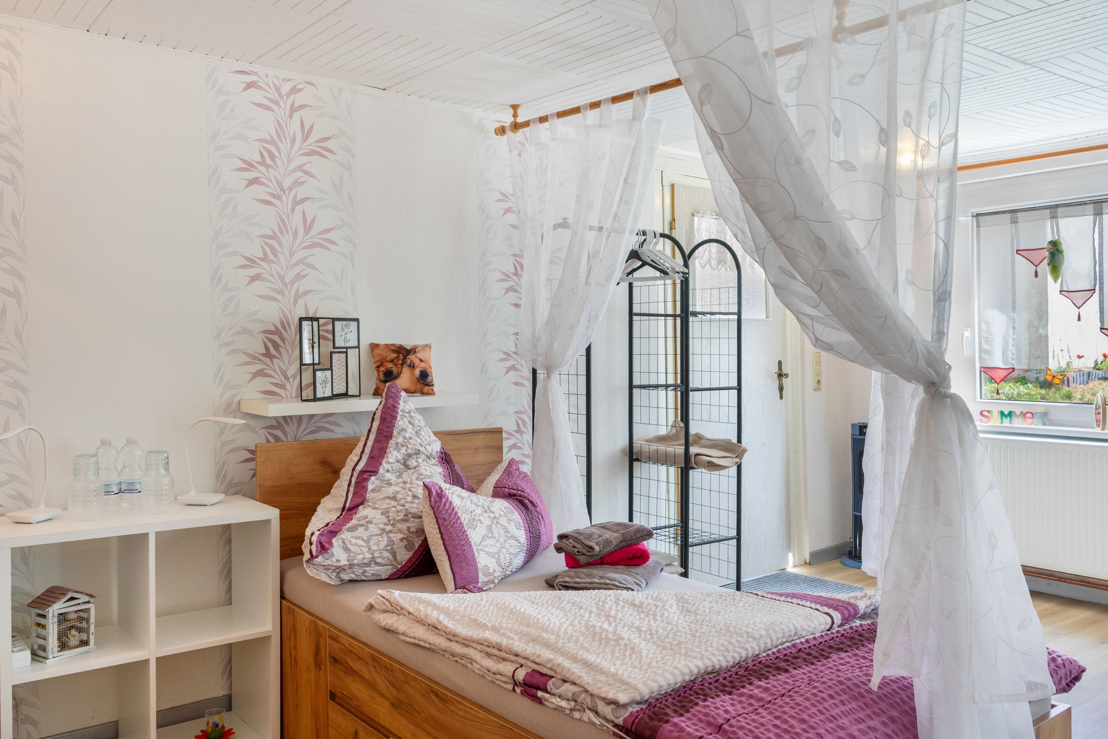 Ein Schlafzimmer mit einem Bett, einem Nachttisch, einem Kleiderschrank, einer Kleiderstange und einem Fenster mit Blick.