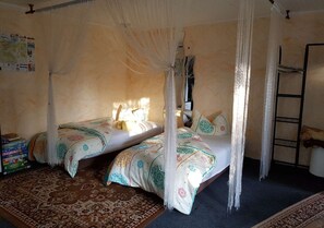 Una habitación con dos camas, mosquitera, escalera y una alfombra estampada.