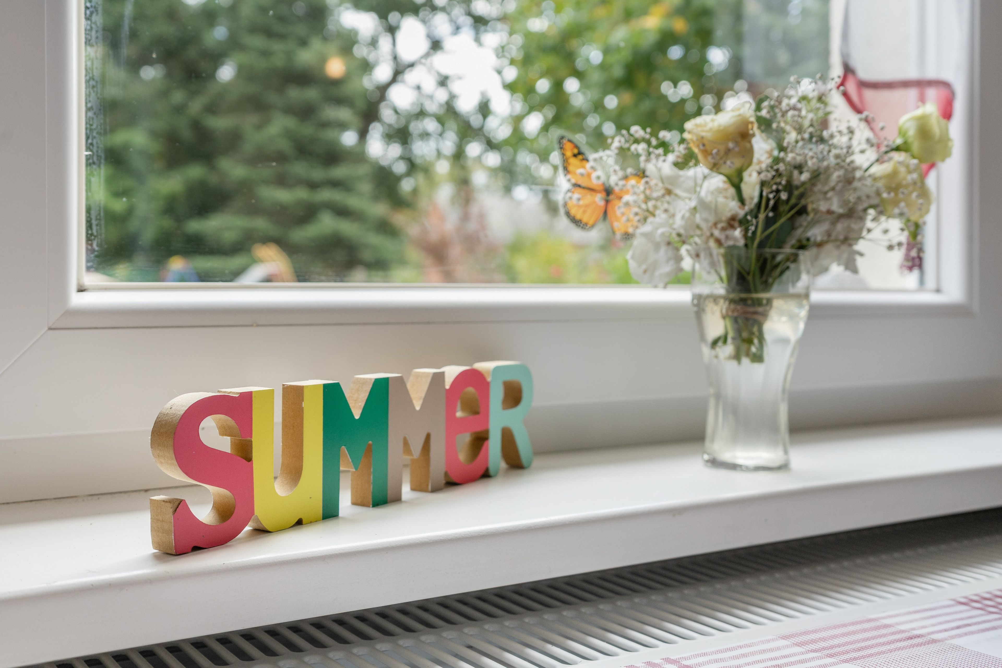 Un alféizar con un jarrón de flores y letras de madera de colores que deletrean 'SUMMER'.