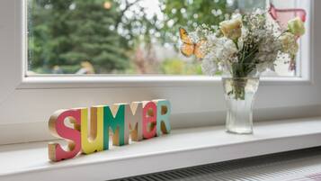 Un alféizar con un jarrón de flores y letras de madera de colores que deletrean 'SUMMER'.