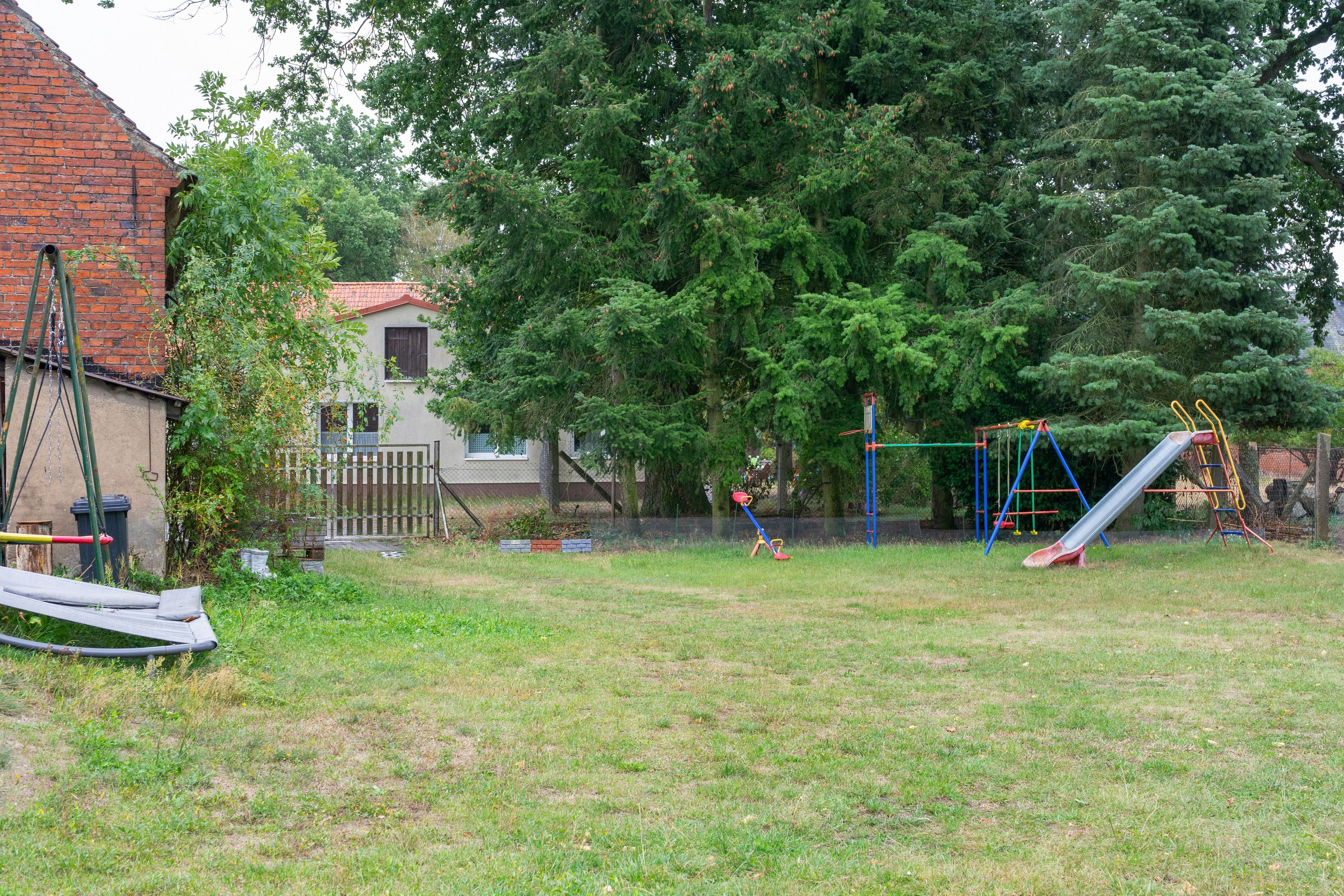 Ein Garten mit Schaukel, Rutsche und einem von Bäumen gesäumten, eingezäunten Bereich.