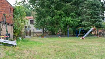 Ein Garten mit Schaukel, Rutsche und einem von Bäumen gesäumten, eingezäunten Bereich.