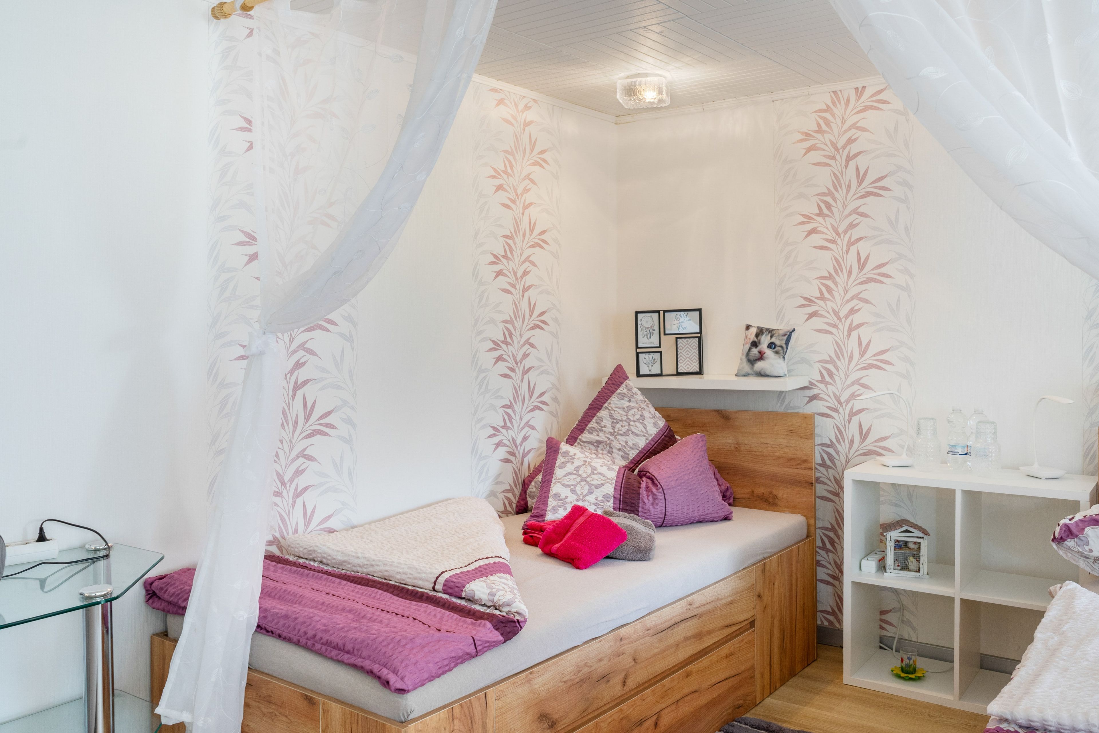 Ein Schlafzimmer mit einem hölzernen Bett, einem Nachttisch, einer Kommode mit gerahmten Bildern und einer Nachttischlampe.