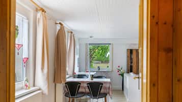 A room with a dining table, chairs, a window with curtains, and a view of greenery outside.