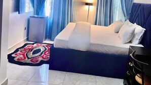 A modern hotel room with a bed, a desk, a TV, and a ceiling light. - Adunola Serviced  Apartment  (Lagos)