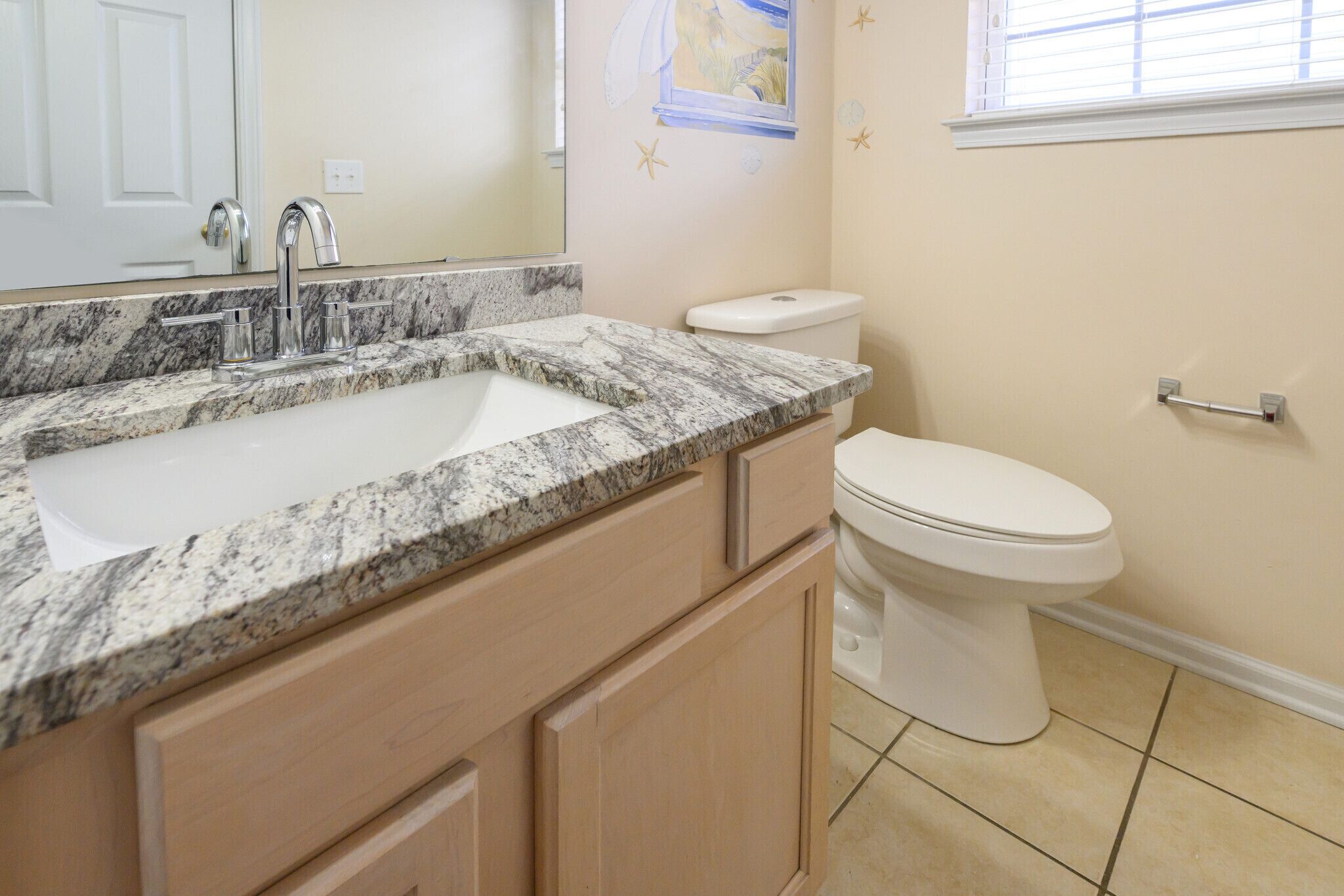 Un baño con lavamanos de encimera de granito, inodoro blanco y paredes color beige.