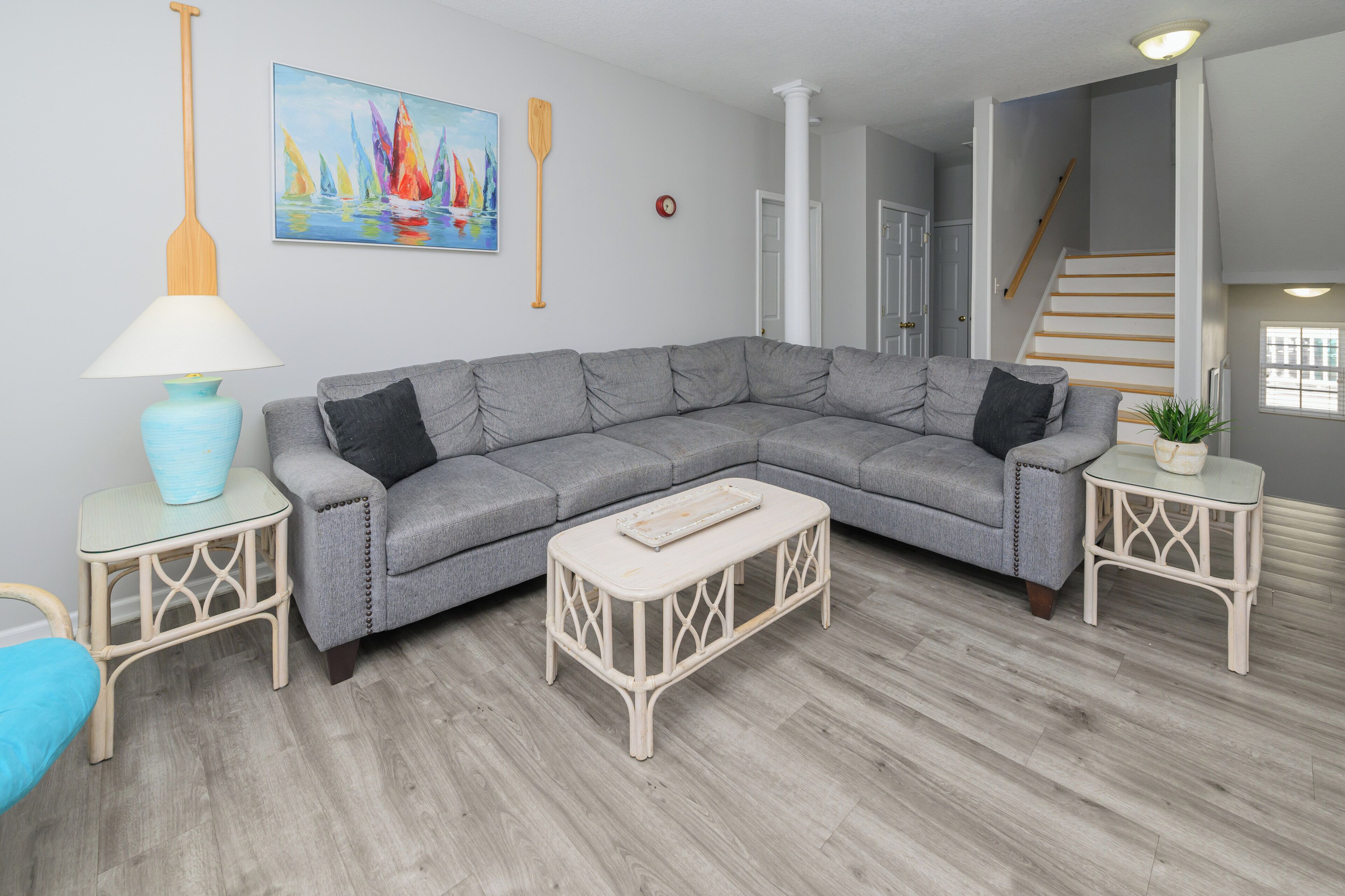Una sala de estar moderna con un sofá seccional gris, una pequeña mesa de centro blanca y una lámpara azul sobre una mesita auxiliar a juego.