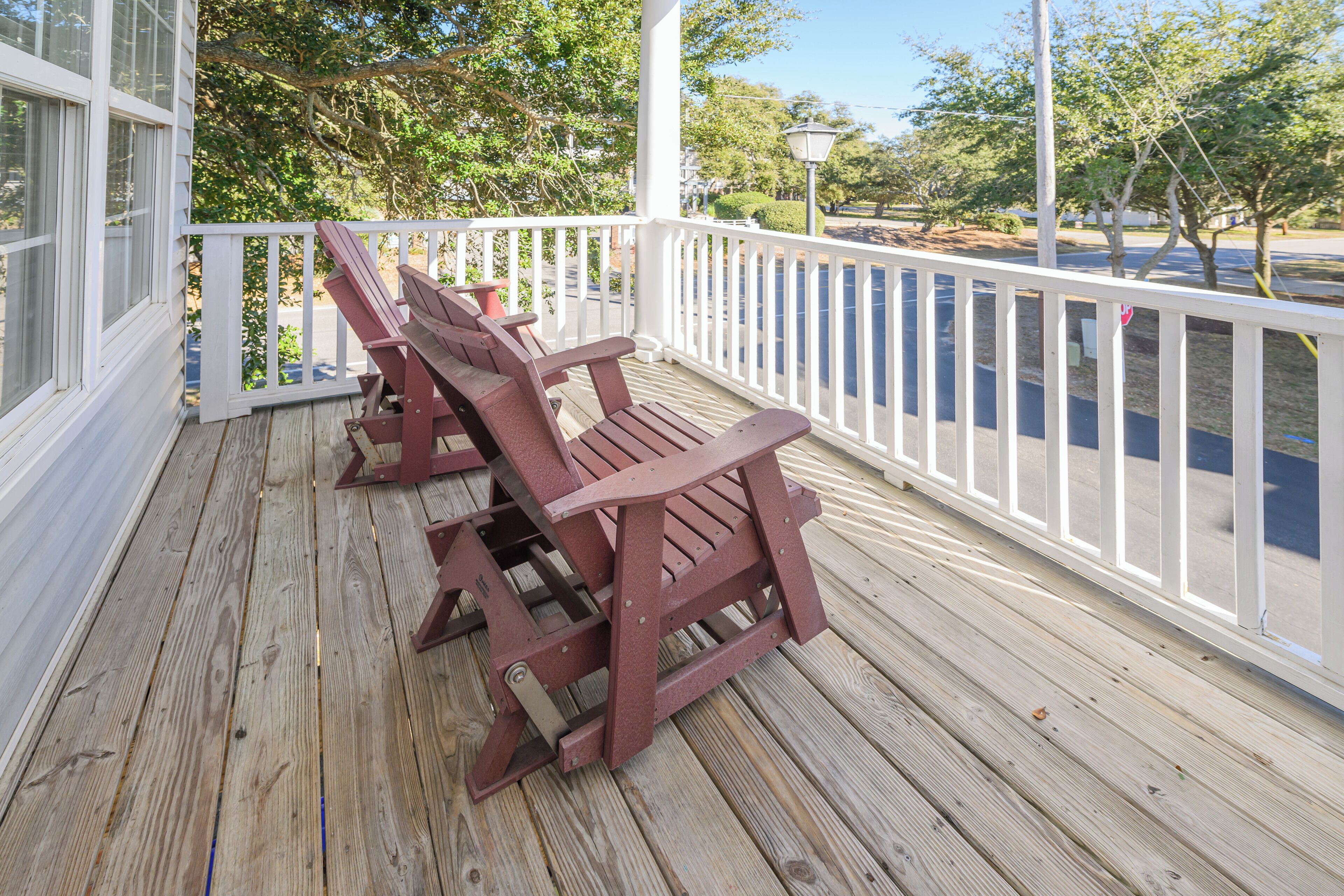 A wooden deck with a white railing and three Adirondack chairs.