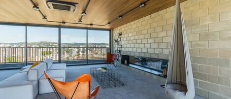 A modern outdoor living area with a sofa, chairs, a hanging chair, and a fireplace.