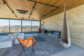 Un espace de vie extérieur moderne comprenant un canapé, des fauteuils, un fauteuil suspendu et une cheminée.