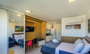 A hotel room with a bed, a desk, a chair, a television, a kitchen area, and artwork on the walls. - Condominium w/ Complete Leisure Facilities and Unbeatable Location in POA - Bles (Porto Alegre)