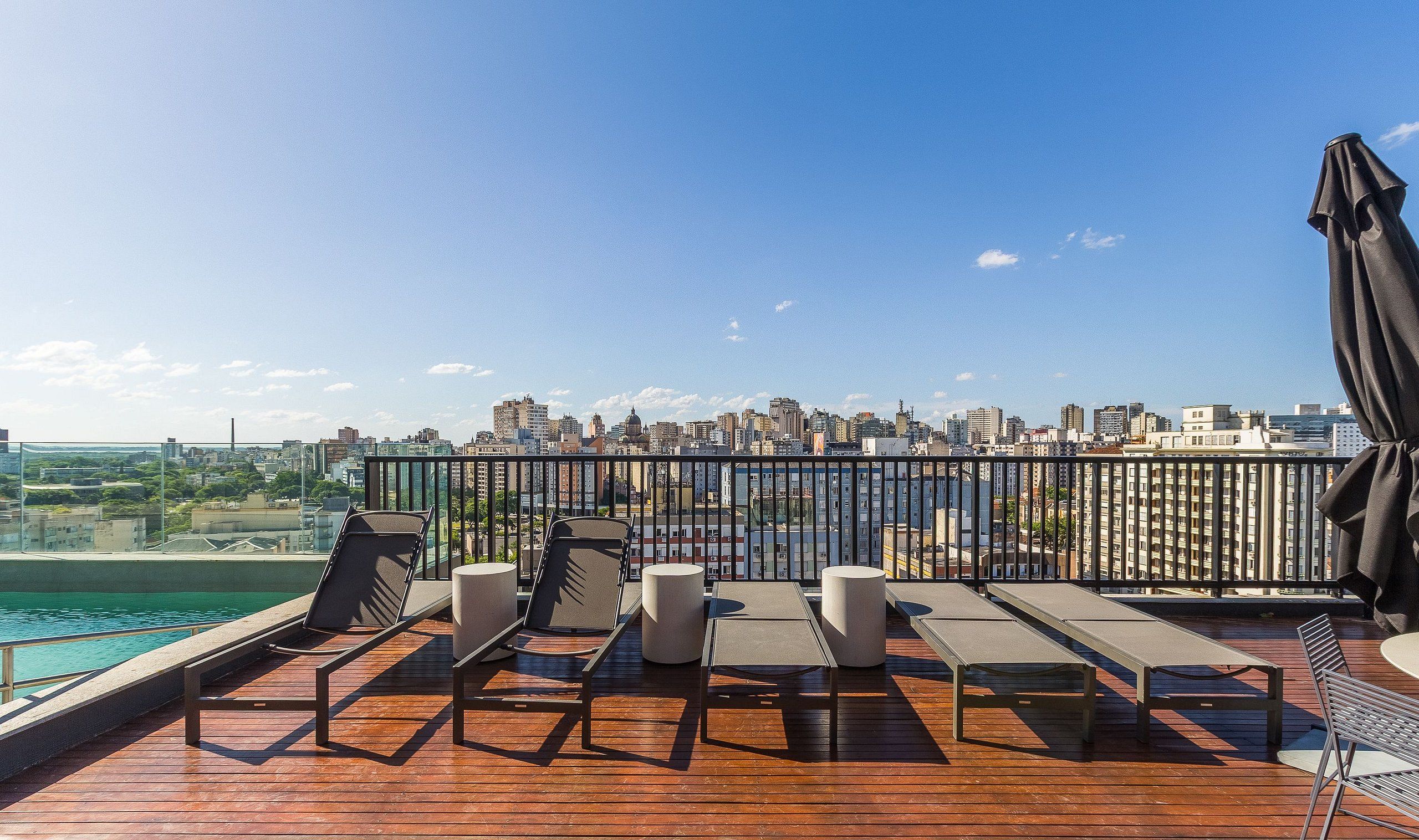 A rooftop terrace with sun loungers, a pool, and a city skyline view.