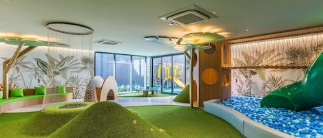 A children's play area with a slide, ball pit, and artificial grass.