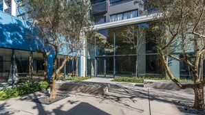 A modern building with large glass windows, a blue facade, and a landscaped area with trees and seating. - Condominium w/ Complete Leisure Facilities and Unbeatable Location in POA - Bles (Porto Alegre)