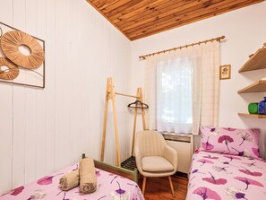 Ein Schlafzimmer mit zwei Betten, einem Sessel, einem Fenster mit Vorhängen und einer Holzbalkendecke.
