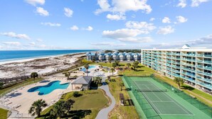 Un complejo turístico con una piscina grande, canchas de tenis y vista al mar.