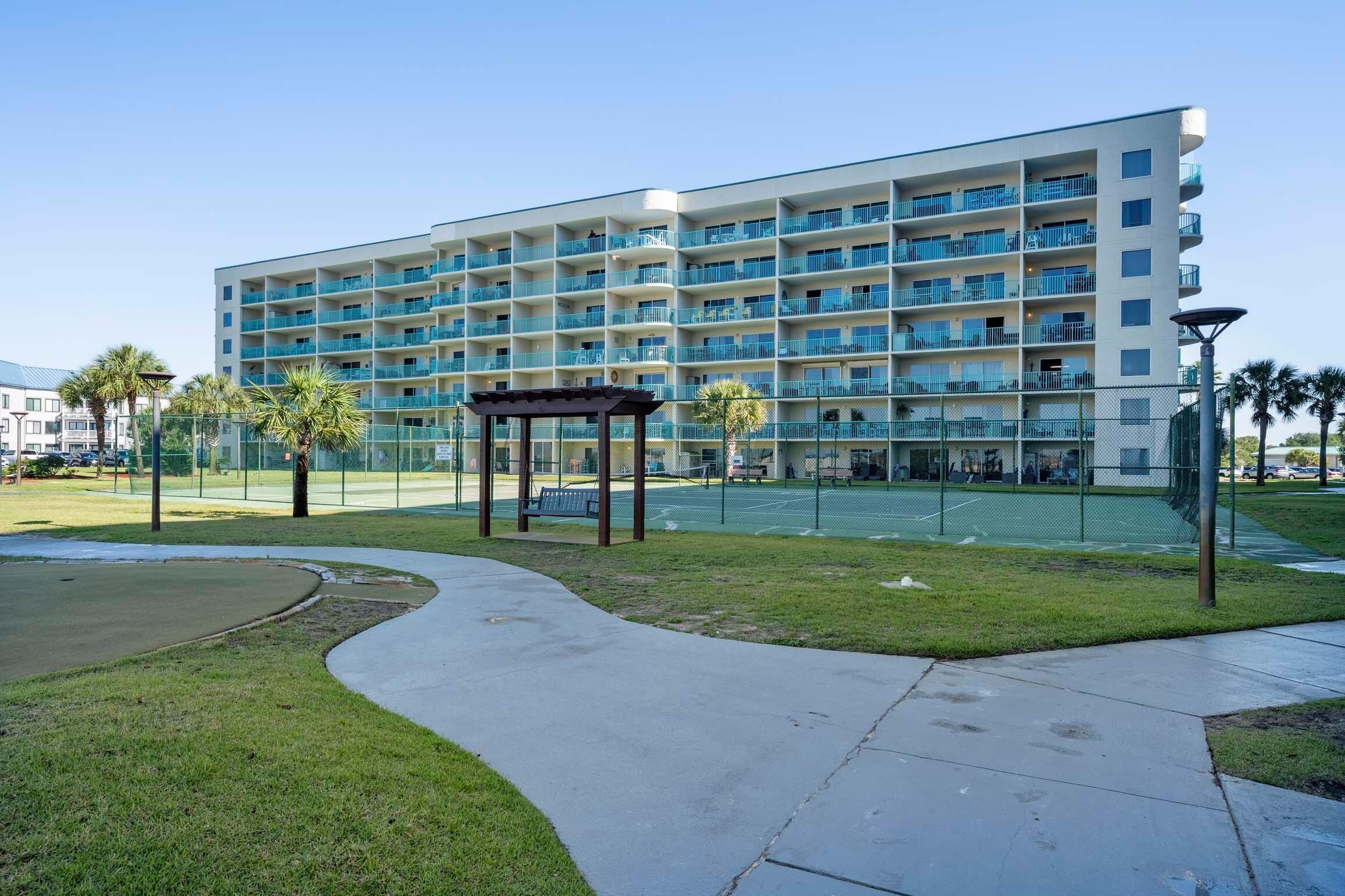 A multi-story hotel with balconies, a covered seating area, and a tennis court.