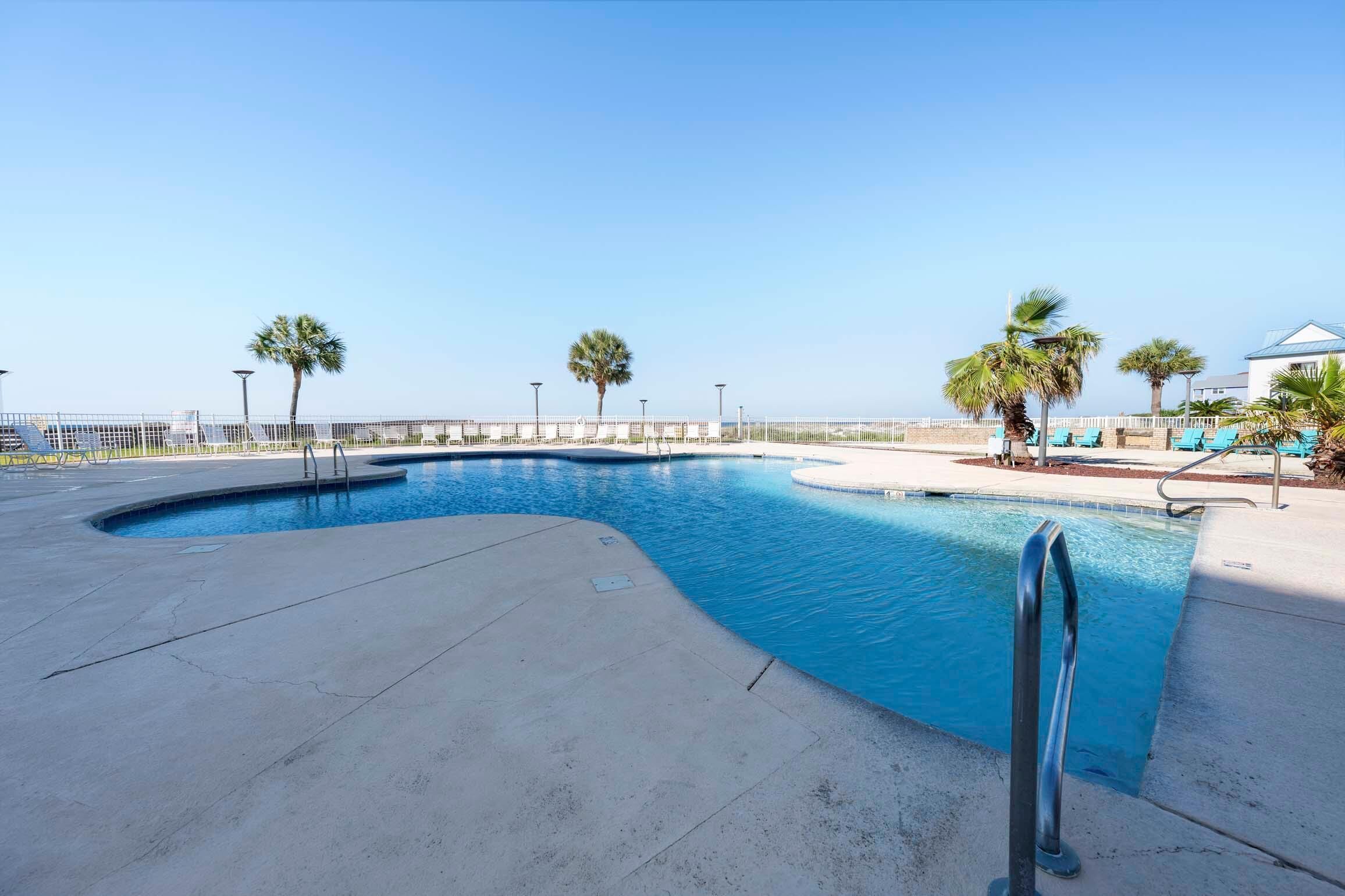 Una piscina de borde curvo, baranda metálica y palmeras.