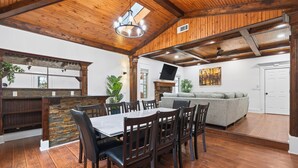 A spacious dining area with a wooden ceiling, a stone accent wall, and a gray sofa in the background. - Mall of GA, Cozy 5 Bedrooms Gateway, Sleep 12 + Game Room and Wi-Fi (Buford)