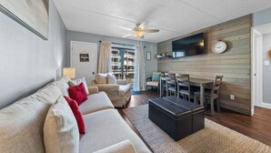 Ein Wohnzimmer mit einer Couch, einem Hocker und einem Essbereich mit Tisch und Stühlen.
