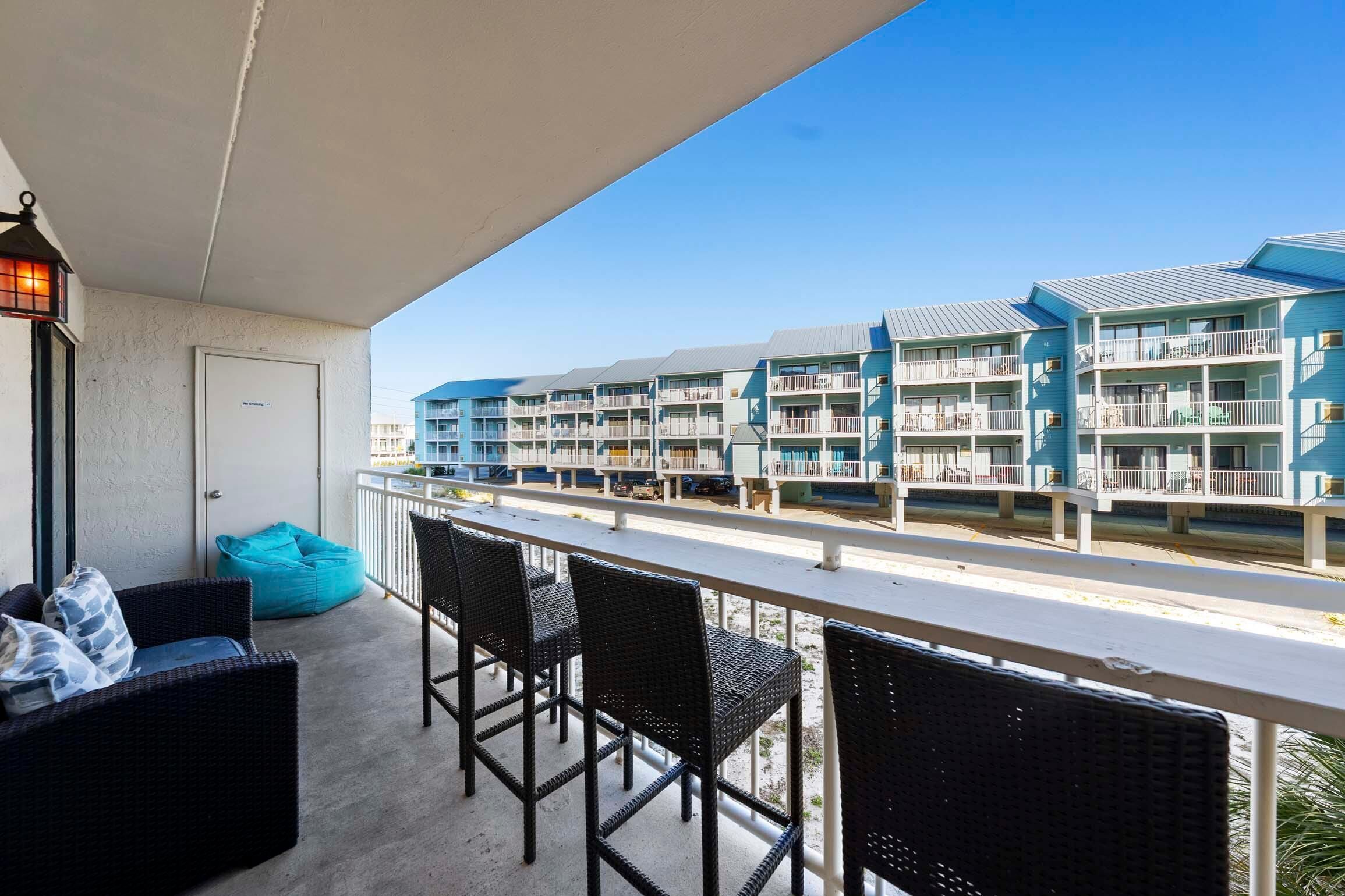 A balcony with wicker furniture, a teal bean bag, and a view of blue multi-story buildings.