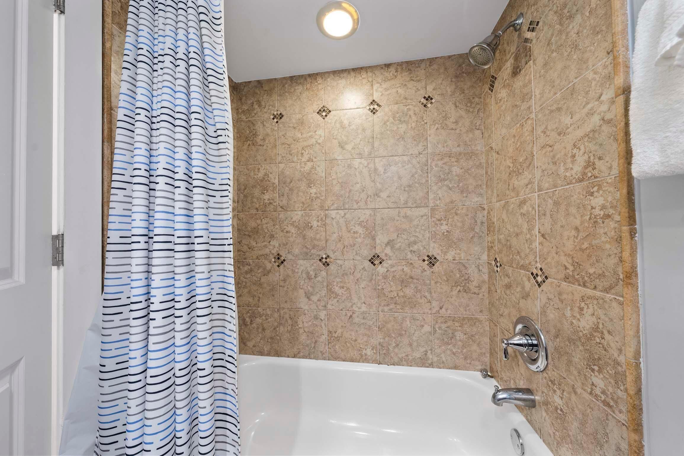 A bathroom with a bathtub, shower, and tiled walls.