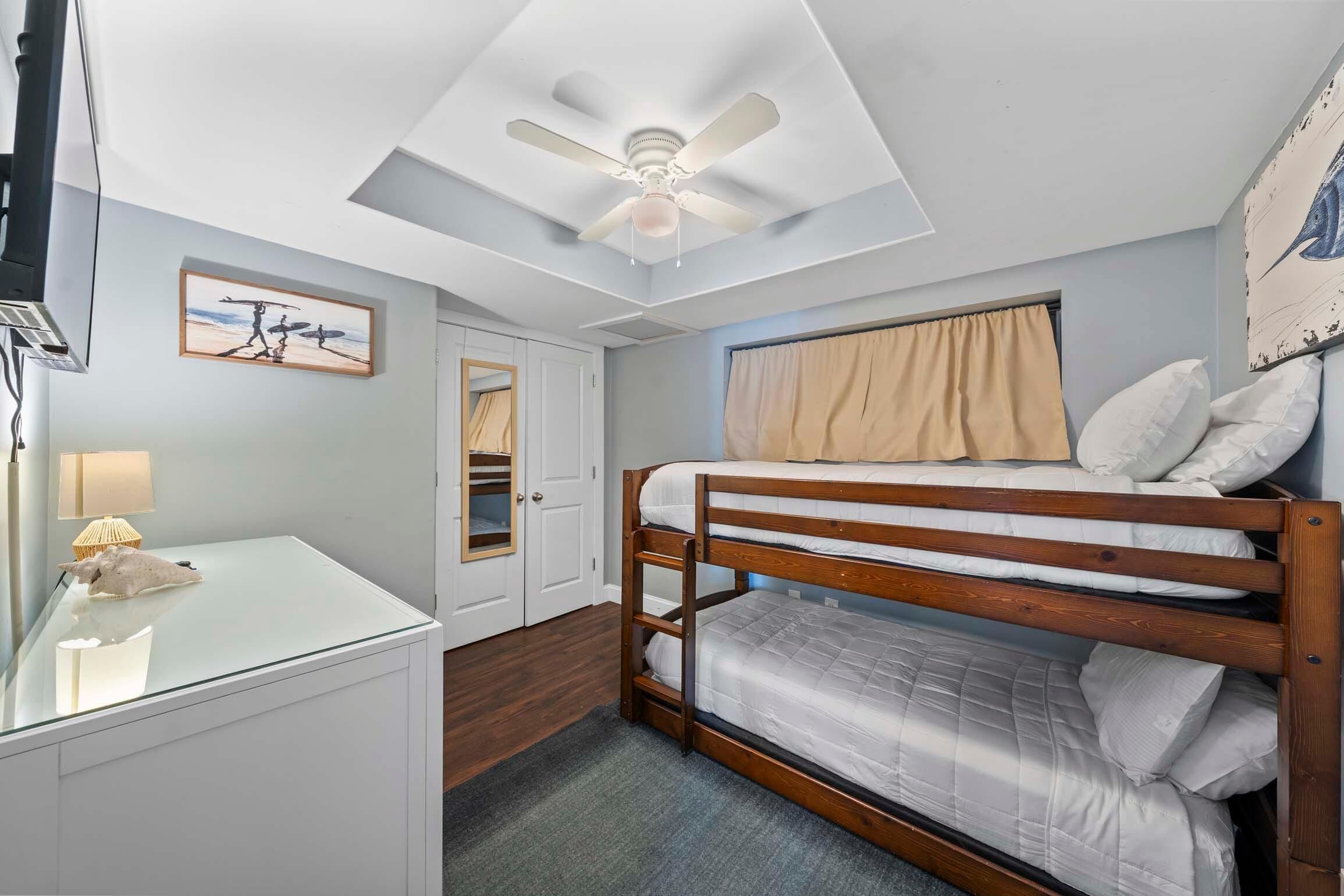 A bedroom with a bunk bed, a desk with a lamp, a ceiling fan, and a window with curtains.