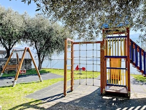 A playground with a swing set, climbing structure, and a fenced area. - Wohnung 'Garden' mit Wasserblick by Interhome (Vercana)