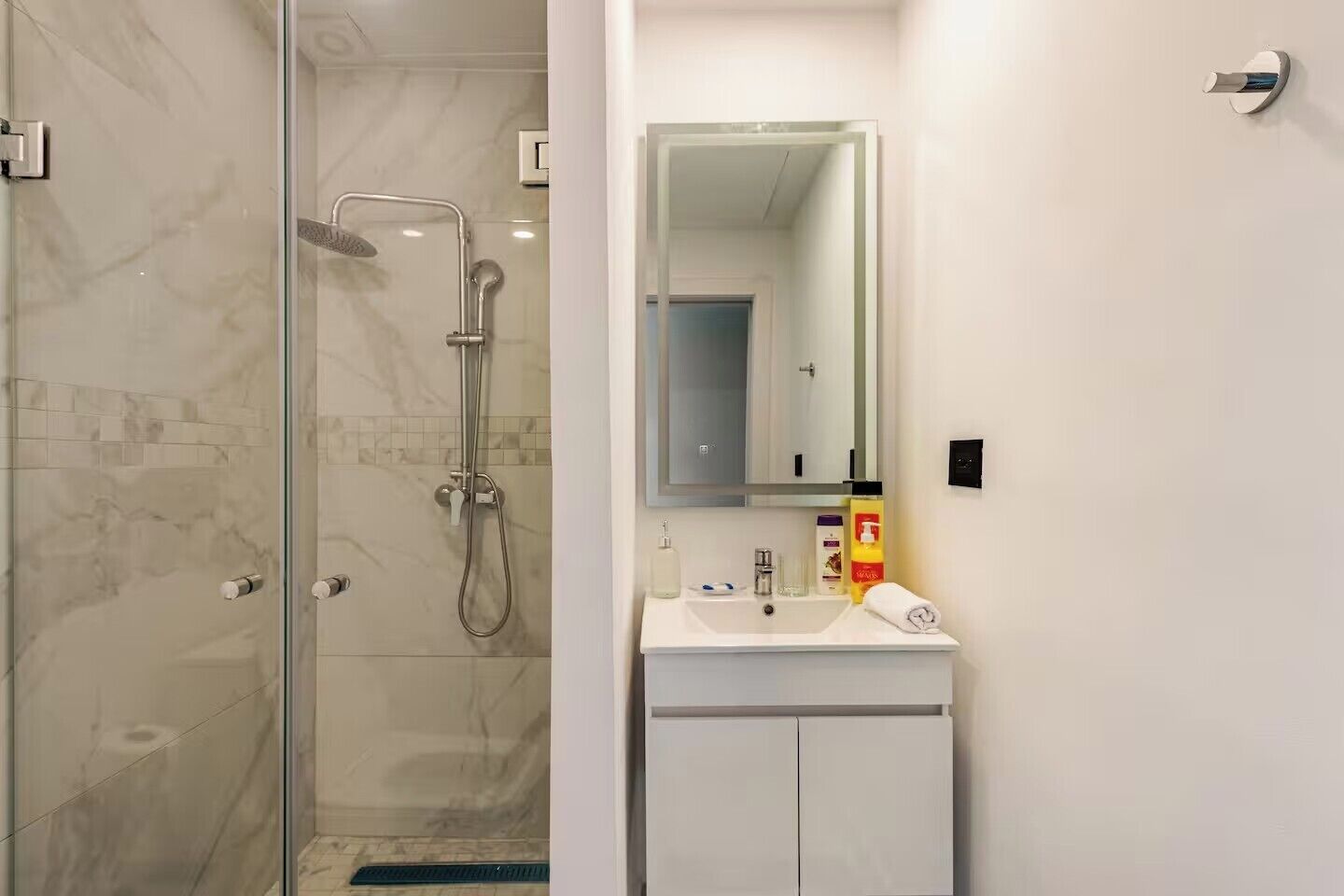 Een moderne badkamer met een douchecabine van glas, een witte wastafel en een spiegel erboven.