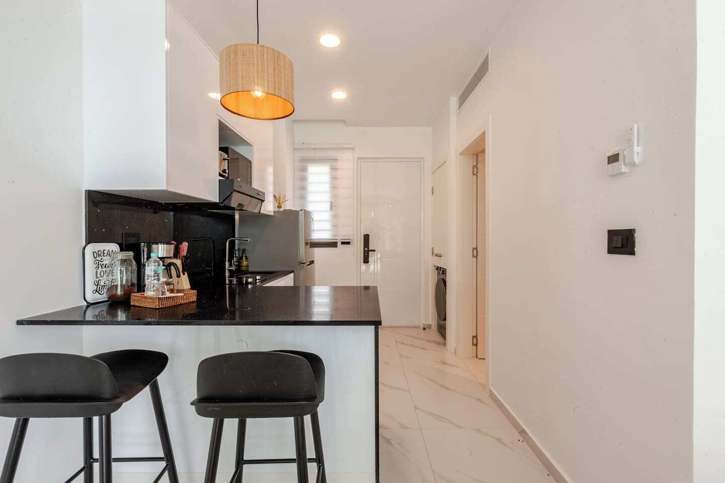 Una cocina moderna con una isla central, dos taburetes de bar y una lámpara colgante.